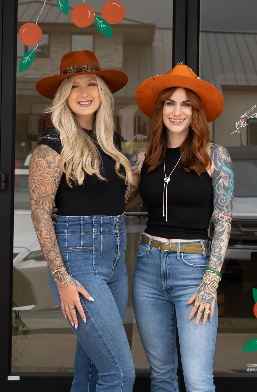 Brittni and Nicolette smiling in orange hats outside the salon entrance
